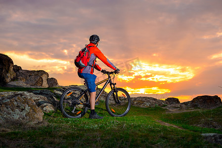 骑山地自行车的骑自行车者在春天的岩石小径上欣赏美丽的日落。