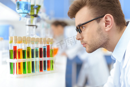 戴眼镜的男科学家在实验室看装有试剂的试管的侧视图