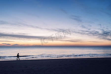 海边夕阳天空摄影照片_日落时沿着海边散步的渔夫
