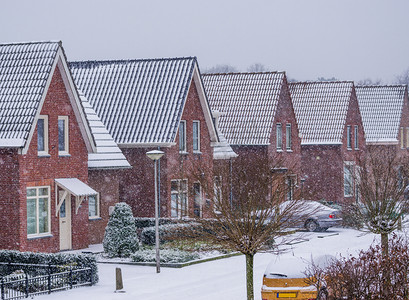 村庄房屋摄影照片_寒冷冬日的现代荷兰社区，荷兰村庄街道上的雪天
