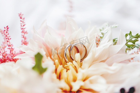 一对金色结婚戒指位于新娘花束中的花朵内。