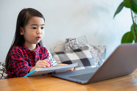 双节放假摄影照片_亚洲女孩或女儿在学校放假期间使用笔记本和技术进行在线学习，并在家观看卡通片。