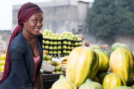 水果架摄影照片_微笑的年轻女子站在水果架之间。