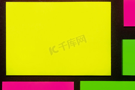 小麻薯贴纸摄影照片_黑纸上的绿色、黄色和紫色色调彩色办公室贴纸。 