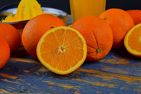 一杯橙汁摄影照片_橘子、橙子、一杯橙汁和蓝色木质背景上的手动柑橘榨汁机。
