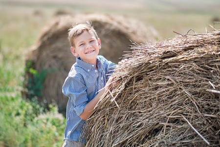 堆摄影照片_坐在干草堆上微笑的迷人男孩