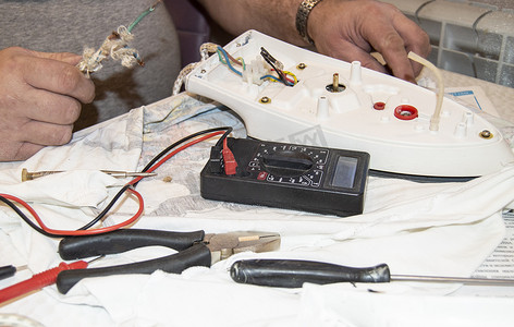 老电工手的特写，使用数字电压表电压修复电熨斗，选择性聚焦