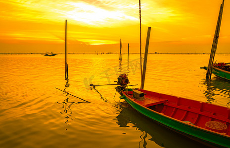 泰国日落时，渔夫的船漂浮在竹竿附近的海中。