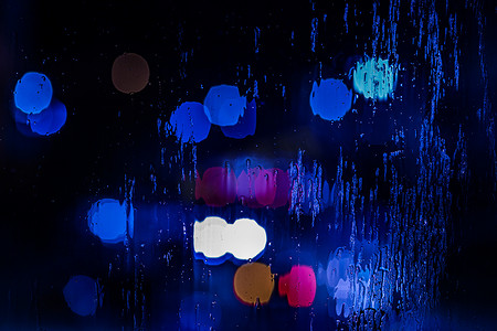 红色和蓝色警灯的抽象背景在夜间通过湿玻璃特写，有选择地聚焦