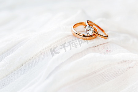 金色钻石摄影照片_带钻石的金色结婚戒指位于白色织物上。