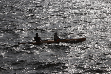 两个人沿着海湾划着皮划艇，在水面上反射出耀眼的阳光。