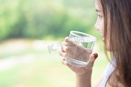 纯净水摄影照片_特写女人从玻璃杯中喝纯净水，玻璃中有光