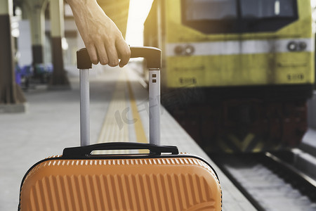 拖着行李旅行摄影照片_拖着橙色手提箱行李袋，走在火车站的女人