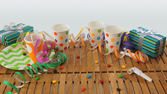 质朴的木桌，上面有五颜六色的彩带、礼品、塑料杯、塑料盘子、白色背景的糖果。