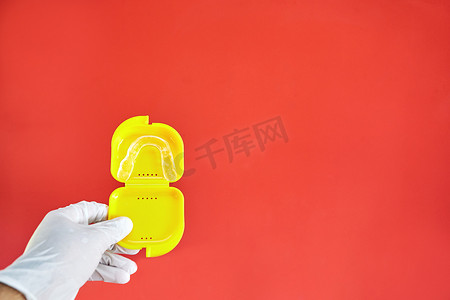 红色背景上黄色表壳中的隐形手镯，一只手拿着乳胶手套