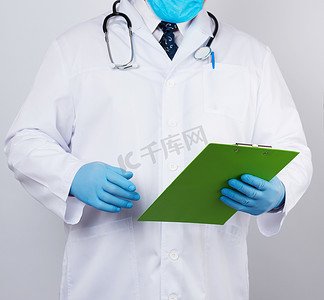 乳汁摄影照片_一件白色外套的男性医生，蓝色乳汁手套，听诊器垂悬