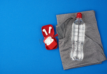折叠灰色运动女 T 恤和蓝色背景上的水瓶
