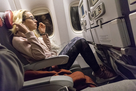 运动休闲的年轻金发白人女士在窗边乘飞机旅行时看电影。