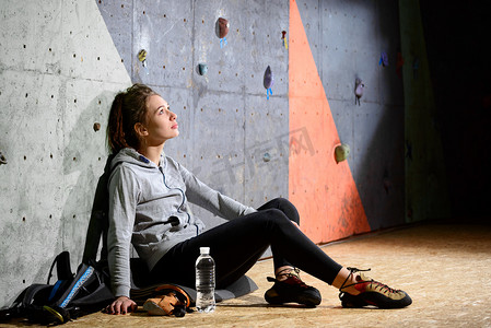 年轻活跃的女性在攀岩馆的人造岩石上抱石后休息。