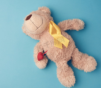 泰迪熊的爪子上拿着一条黄色丝带，上面折成一圈