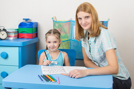 小女孩和一个五岁的女孩坐在一张桌子旁，处理拼写