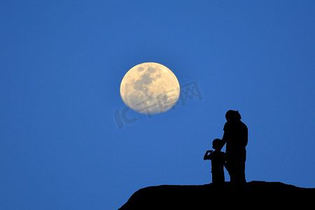 剪影月亮摄影照片_母子站在山上看着的剪影