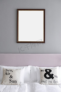 生活方摄影照片_在一间灰色和玫瑰色的极简主义卧室里，挂在床上方墙上的相框模型。