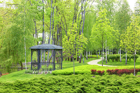 镂空灯笼摄影照片_带有锻造元素的镂空金属凉亭，周围环绕着带景观设计的美丽春天公园。