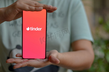 助航标志摄影照片_印度新德里，2020 年。女孩在女性手中的智能手机屏幕上拿着带有 Tinder 标志的手机。 