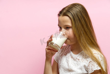 扎着辫子和牛奶胡子的女孩在粉红色的背景下喝牛奶。