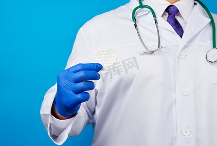 乳汁摄影照片_一件白色外套的男性医生，拿着一个的蓝色乳汁医疗手套
