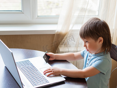 好奇的蹒跚学步的男孩探索笔记本电脑并按下电脑键盘上的按钮。