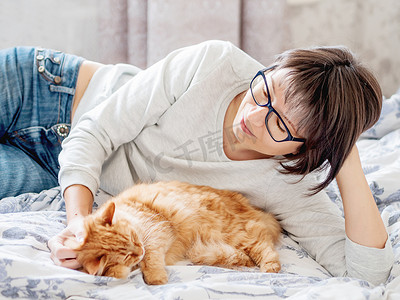 可爱的姜猫和戴眼镜的女人躺在床上。
