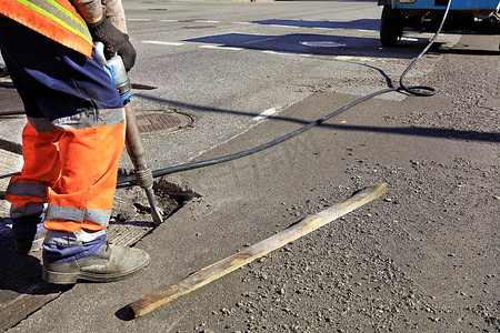 一名工人在道路施工中用气动手提钻清理一块沥青。