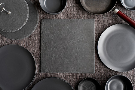 陶瓷器皿摄影照片_成堆的黑色陶瓷盘子和灰色背景中的餐具顶视图