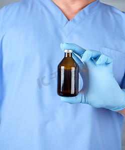 乳汁摄影照片_蓝色制服和乳汁手套的医生拿着一个棕色玻璃bo