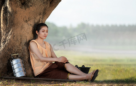 一位美丽的泰国女人坐在树下放松，因 w 疲倦