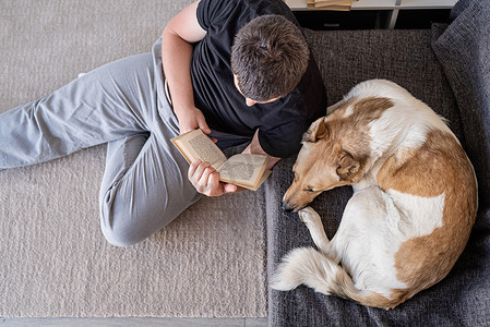 年轻人和他的狗坐在家里的地板上看书