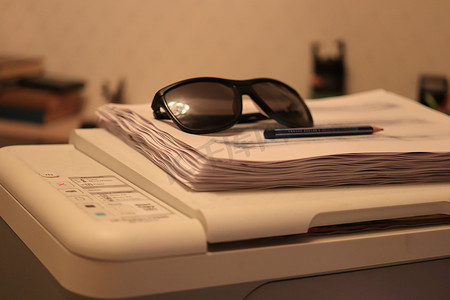 带笔的太阳镜躺在打印机上的一叠纸上
