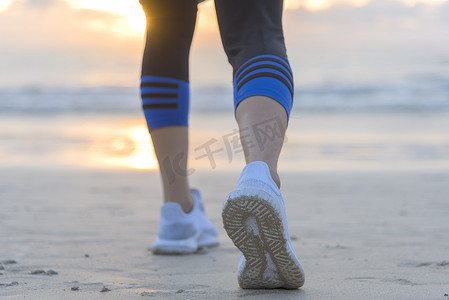 女人在日出时在沙滩上跑步，特写是鞋子。
