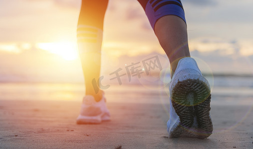 鞋子背摄影照片_女人在日出时在沙滩上跑步，特写是鞋子。