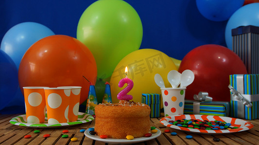 青色摄影照片_在土气木桌上的生日蛋糕有五颜六色的气球、礼物、塑料杯子和塑料盘子的背景有糖果和蓝色墙壁的在背景中