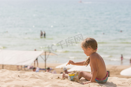 五岁小女孩坐在沙滩上，在大海的背景下玩沙子和玩具