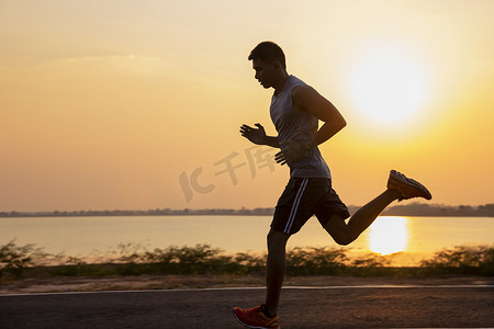 在公路上奔跑摄影照片_夏日日落时分，英俊的年轻人在乡村公路上奔跑
