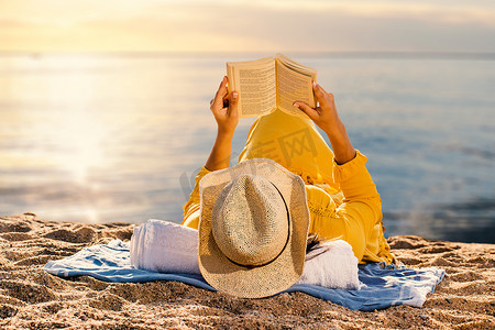 日落时在海滩上读小说的女人。
