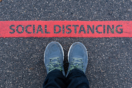 social摄影照片_穿着运动鞋的男人站在一条红线旁边，上面写着 SOCIAL DIS