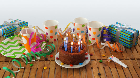 巧克力生日蛋糕，蓝色蜡烛在质朴的木桌上燃烧，背景是五颜六色的彩带、礼物、塑料杯和糖果，背景是白墙