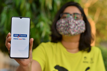 印度新德里，2020 年。在冠状病毒 (Covid-19) 疾病大流行期间，戴着面罩的女孩展示 Yes bank 应用程序。