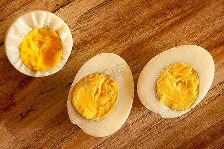 煮熟的鸡蛋摄影照片_煮熟的鸡蛋，在木质背景上切成两半