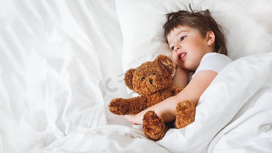 蹒跚学步的孩子和可爱的泰迪熊躺在床上。